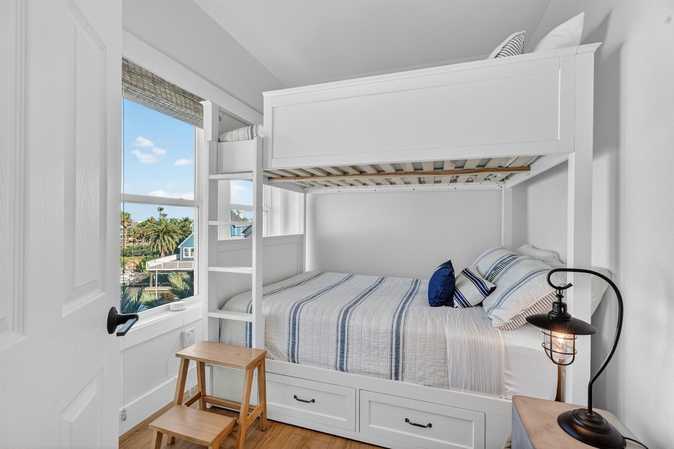 Built-in bunk bedroom with ladder, storage drawers, window views, and coastal striped bedding.