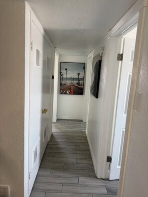 A hallway with a wooden floor, white walls, and a door at the end leading to a room. - Cozy Home with refrigerated AC with easy access near malls & freeway. (El Paso)