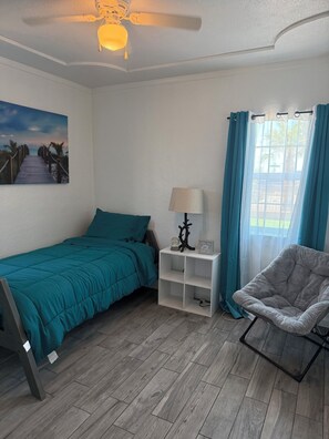 A bedroom with a bed, a nightstand, a chair, a ceiling fan, a window with curtains, and a wall-mounted lamp. - Cozy Home with refrigerated AC with easy access near malls & freeway. (El Paso)