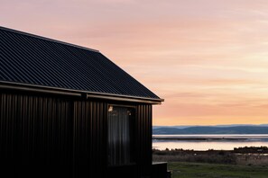 Een gebouw met een schuin dak en een groot raam, met uitzicht op een waterpartij en heuvels in de verte.