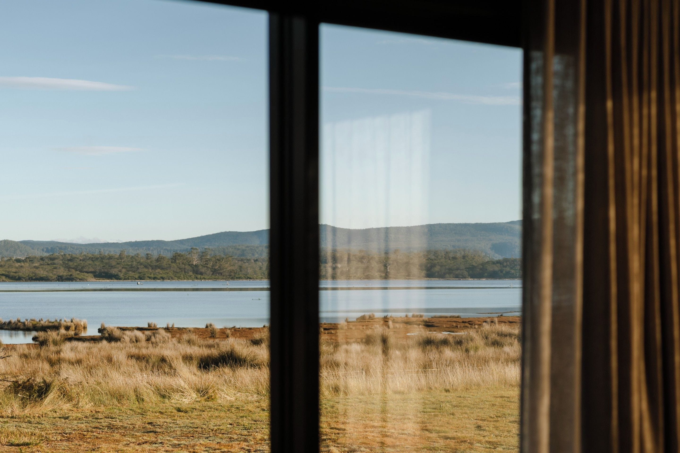 A view through a window of a natural landscape with a body of water, grassy areas, and distant hills.