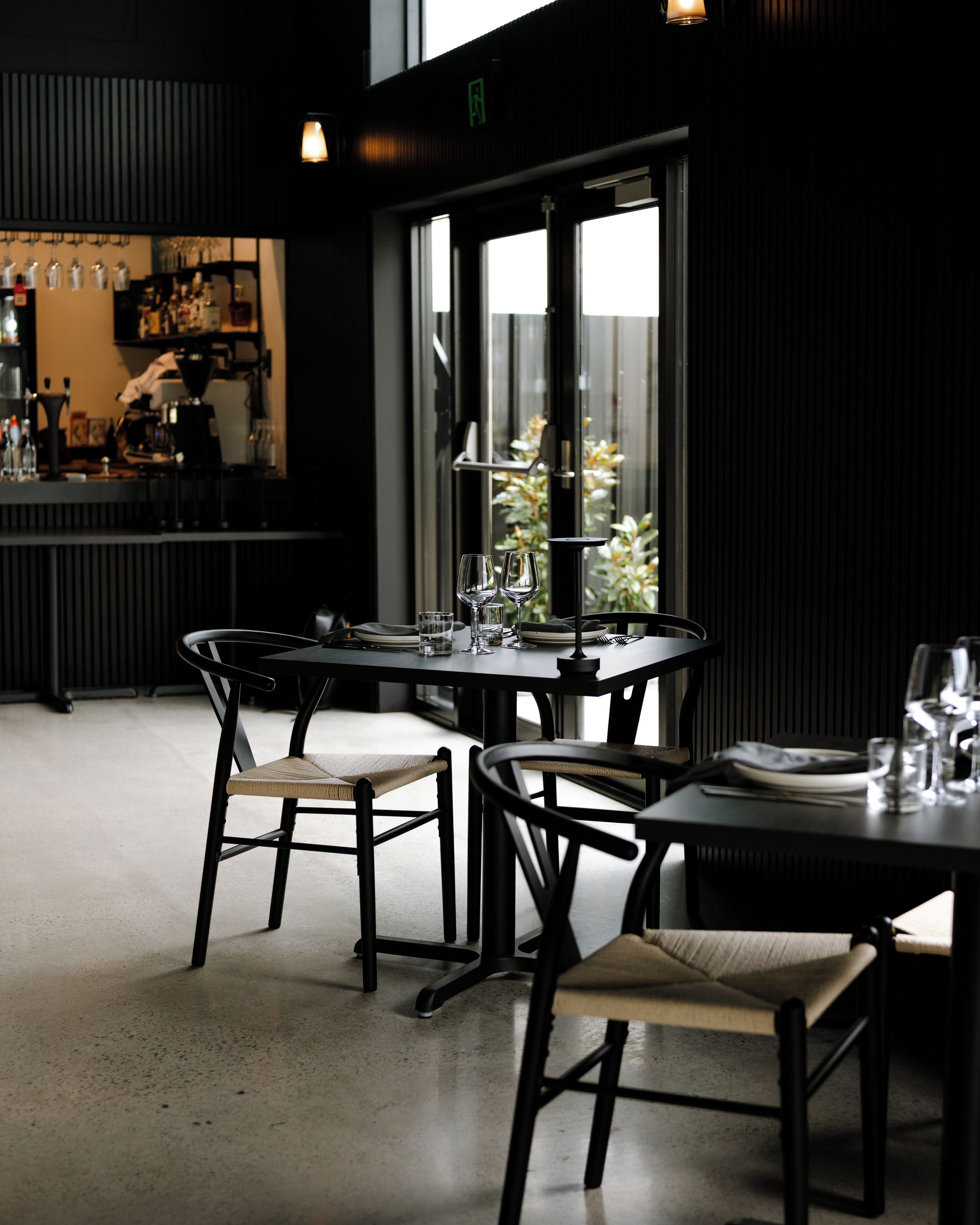 A restaurant interior with a bar area, dining tables, chairs, and a view of greenery outside.