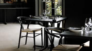 A restaurant interior with a bar area, dining tables, chairs, and a view of greenery outside.