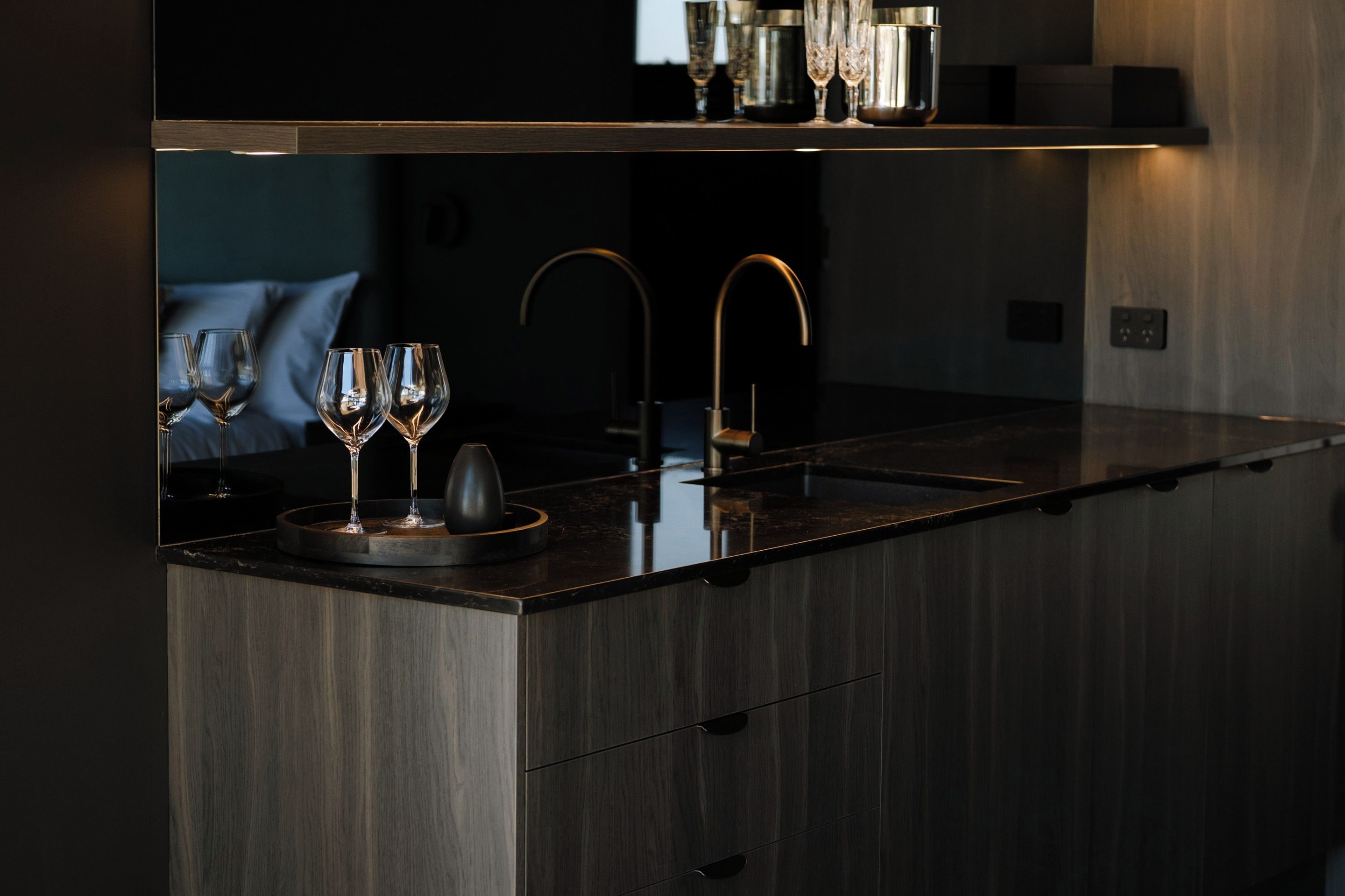 A modern kitchen with a dark countertop, a built-in sink, and a wine glass holder.