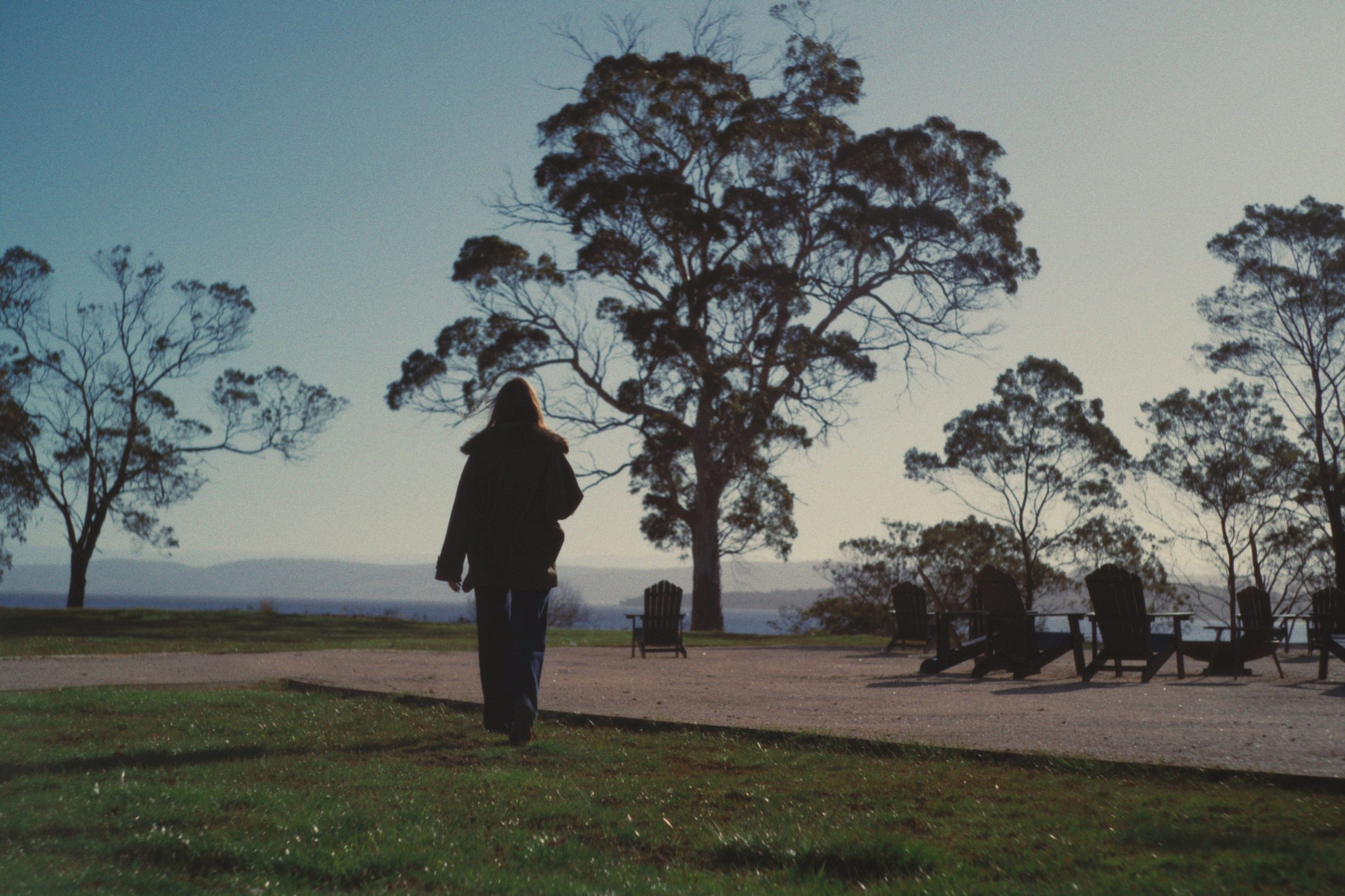 A person walking on a path in a park with trees and benches.