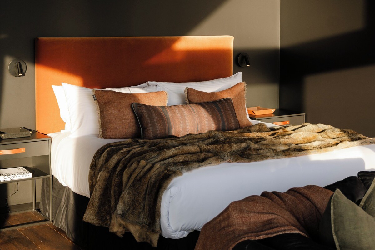 Een netjes opgemaakt bed met een bruine vachtdeken, witte kussens en een bruin hoofdbord.
