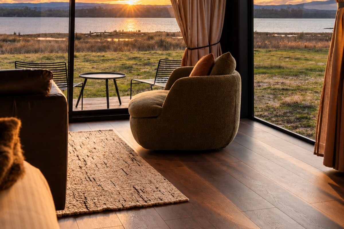 Een modern interieur met een groot raam met uitzicht op een natuurlandschap bij zonsondergang.