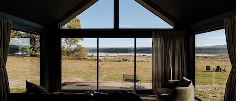 Un dormitorio con un ventanal grande que da a un campo verde y un lago.
