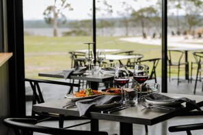 Un área de comedor al aire libre con mesas preparadas para dos comensales, cada una con un plato de comida, vasos y cubiertos.