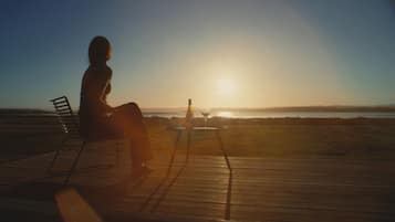 A person sitting on a chair on a wooden deck overlooking a body of water during sunset.