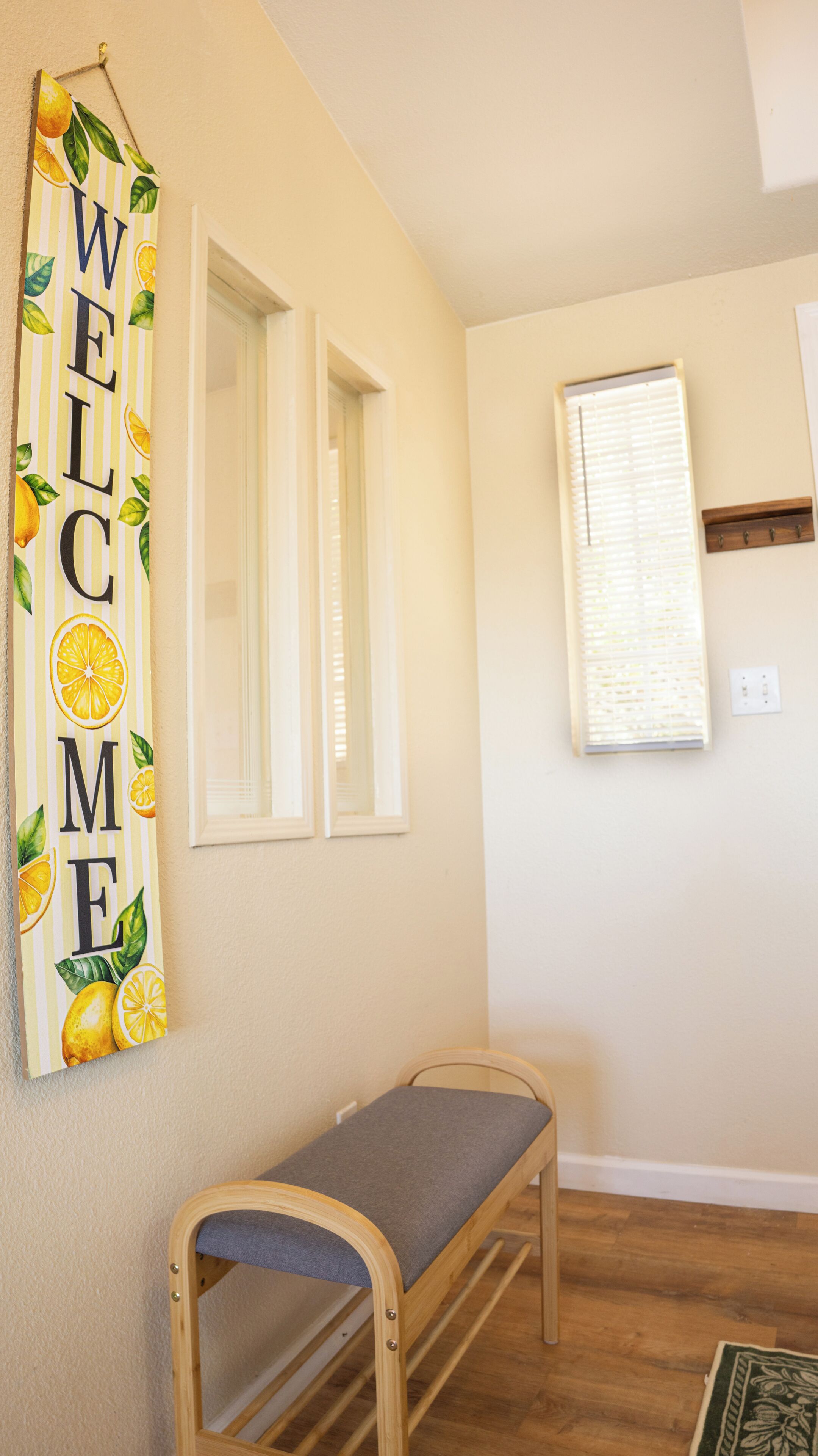 A room with a wooden bench, a wall-mounted welcome sign, and a window with blinds.