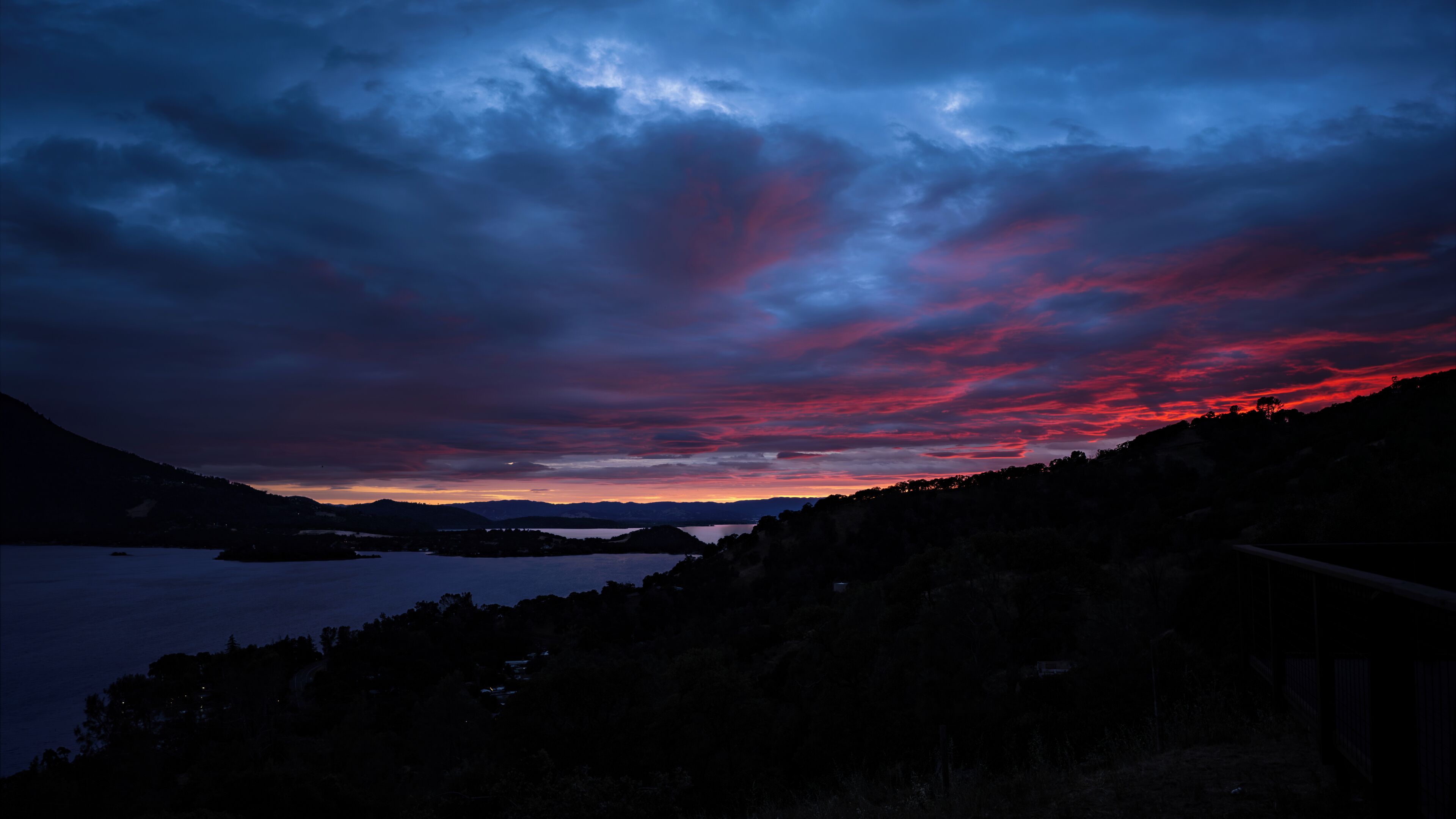 A landscape with a body of water, hills, and a cloudy sky.