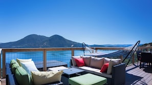 Una terraza con asientos al aire libre, una hamaca y vistas a las montañas y al agua.