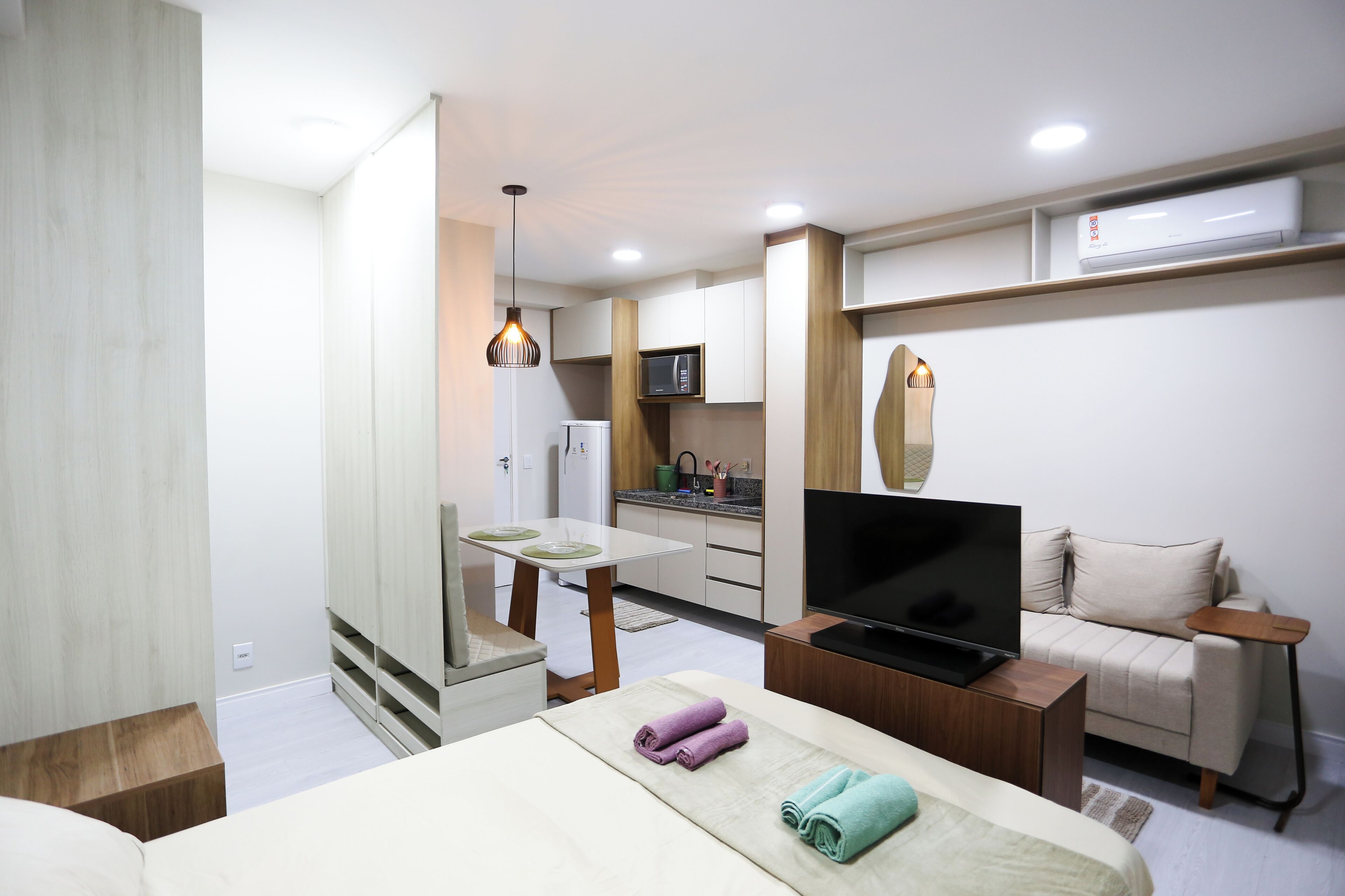 A hotel room with a bed, a TV, a sofa, a small table, and a kitchenette.