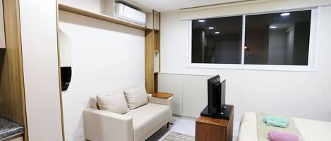 Un dormitorio moderno con sofá, cama, televisión y ventana.