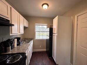 Una cocina funcional con estufa, pileta y refrigerador, que cuenta con una ventana y una puerta.