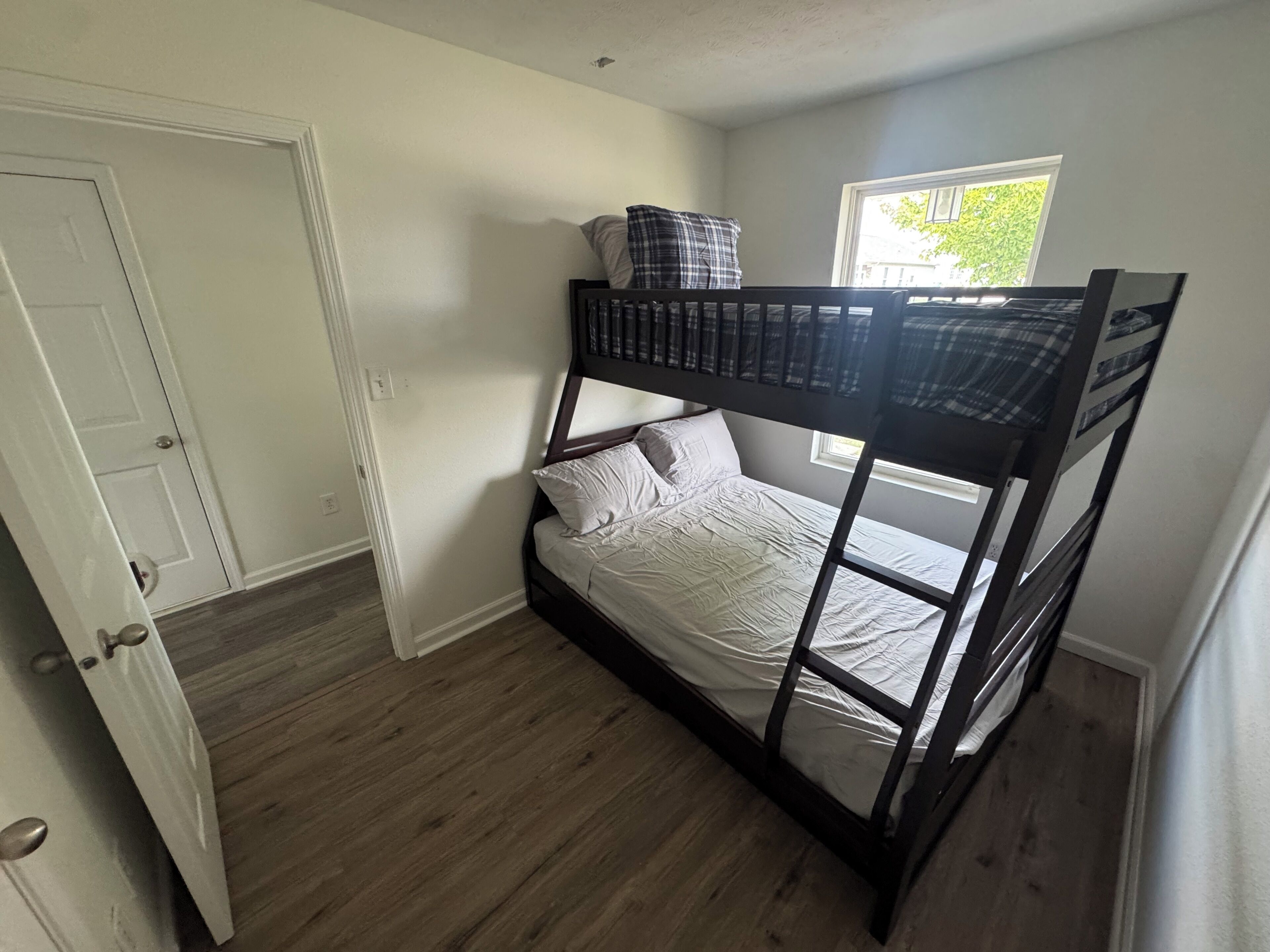 A bunk bed room with a door, a window, and a view of greenery outside.