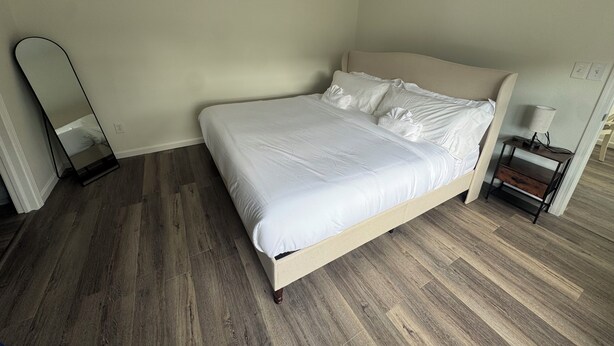Een slaapkamer met een bed, nachtkastje, spiegel en plafondventilator.
