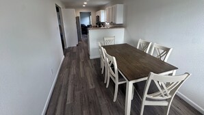 Een smalle gang die uitkomt op een eetruimte met een houten tafel en witte stoelen.