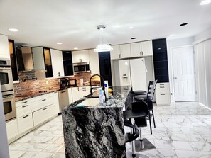 A modern kitchen with white cabinets, a granite island, and a stainless steel refrigerator.