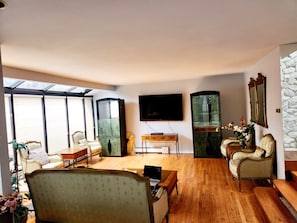 A spacious living room with a large TV, wooden flooring, and a view through a skylight.