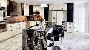 A modern kitchen with white cabinets, a granite countertop, a stainless steel oven, a microwave, a refrigerator, and a bar area with stools. - Beautiful 5-bedroom house with AC in wonderful Bay Shore (Bay Shore)