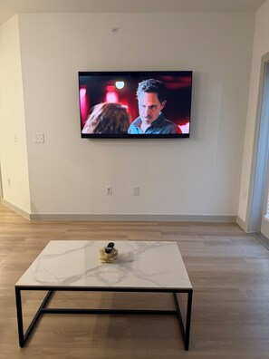 Ein an der Wand befestigter Fernseher mit einer Fernbedienung auf einem Tisch mit Marmorplatte davor.