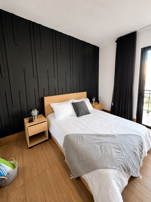 A modern bedroom with a wooden headboard, a large bed with white bedding, a grey throw blanket, and a nightstand with a lamp. - MAREA | Prestige Suite (Punta Cana)