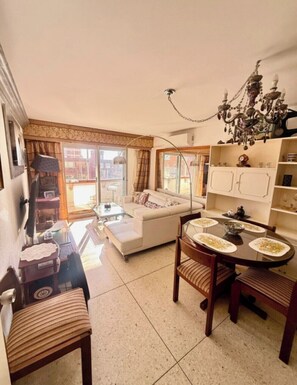 A living room with a sofa, a dining table with chairs, a chandelier, and a view of the outside. - 2-bedroom apartment in fabulous Punta del Este with AC and gym (Punta del Este)