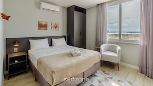 Ett hotellrum med en säng, en stol, en luftkonditionering, ett nattduksbord och ett fönster med utsikt.