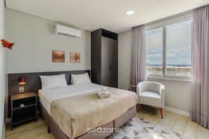 A hotel room with a bed, a chair, an air conditioner, a nightstand, and a window with a view. - Studio w/ Pool Close to Ccmq Tco1008 (Porto Alegre)