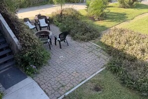 Een terras met vuurkorf, buitenmeubels en omliggende begroeiing.