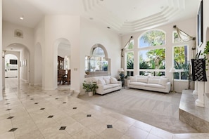 A spacious living area with a large white sofa, a dining table, and a kitchen in the background.