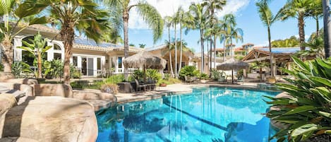 A pool surrounded by palm trees and a building with a tiled roof.
