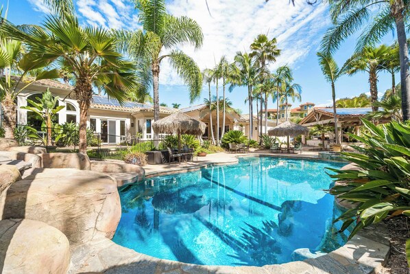 A pool surrounded by palm trees and a building with a tiled roof.