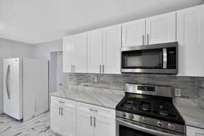 A modern kitchen with white cabinets, a stainless steel microwave, a gas stove, and a refrigerator.