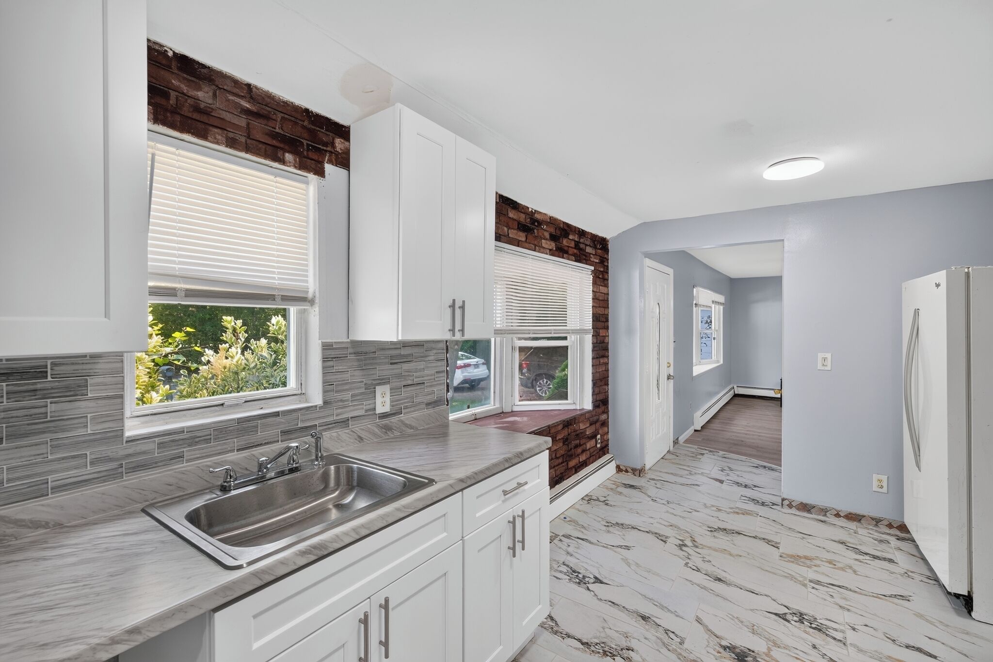 A modern kitchen with white cabinets, a stainless steel sink, and a view of the outdoors through a window.