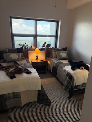 Ein Schlafzimmer mit zwei Betten, einem Fenster mit Blick und einer Lampe. Auf einem Bett liegt ein Stofftier.