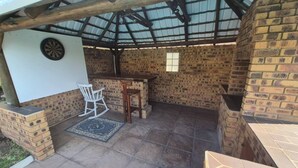 A covered outdoor area with a brick wall, a table, two chairs, and a dartboard. - Room-nombelas Cottage (Westville)