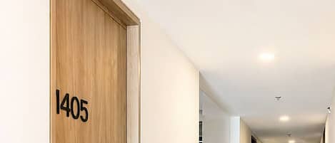 A long, narrow hotel corridor with a wooden door labeled '1405' on the left, leading to a room.