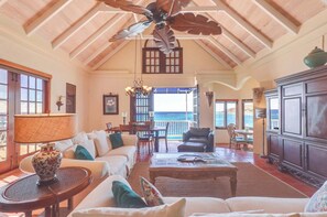 Un'ampia zona giorno con soffitto alto, ventilatore a soffitto, vista sull'oceano e zona pranzo con tavolo e sedie.
