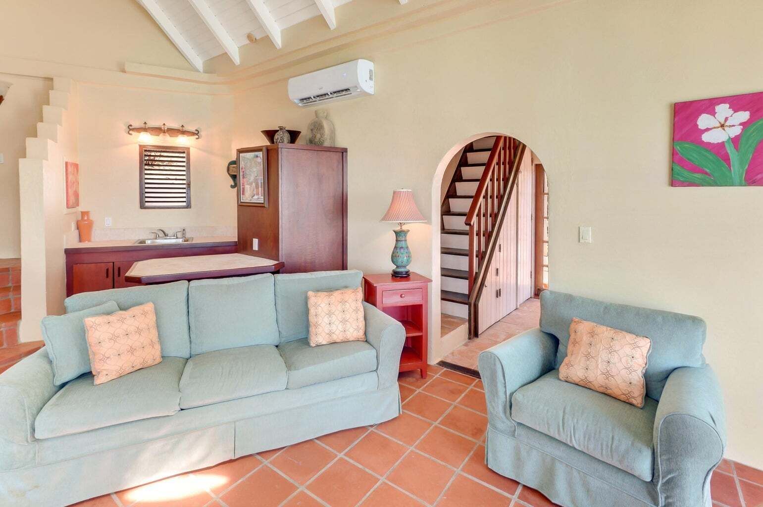 A living room with a sofa, a chair, a lamp, a painting, and a staircase.
