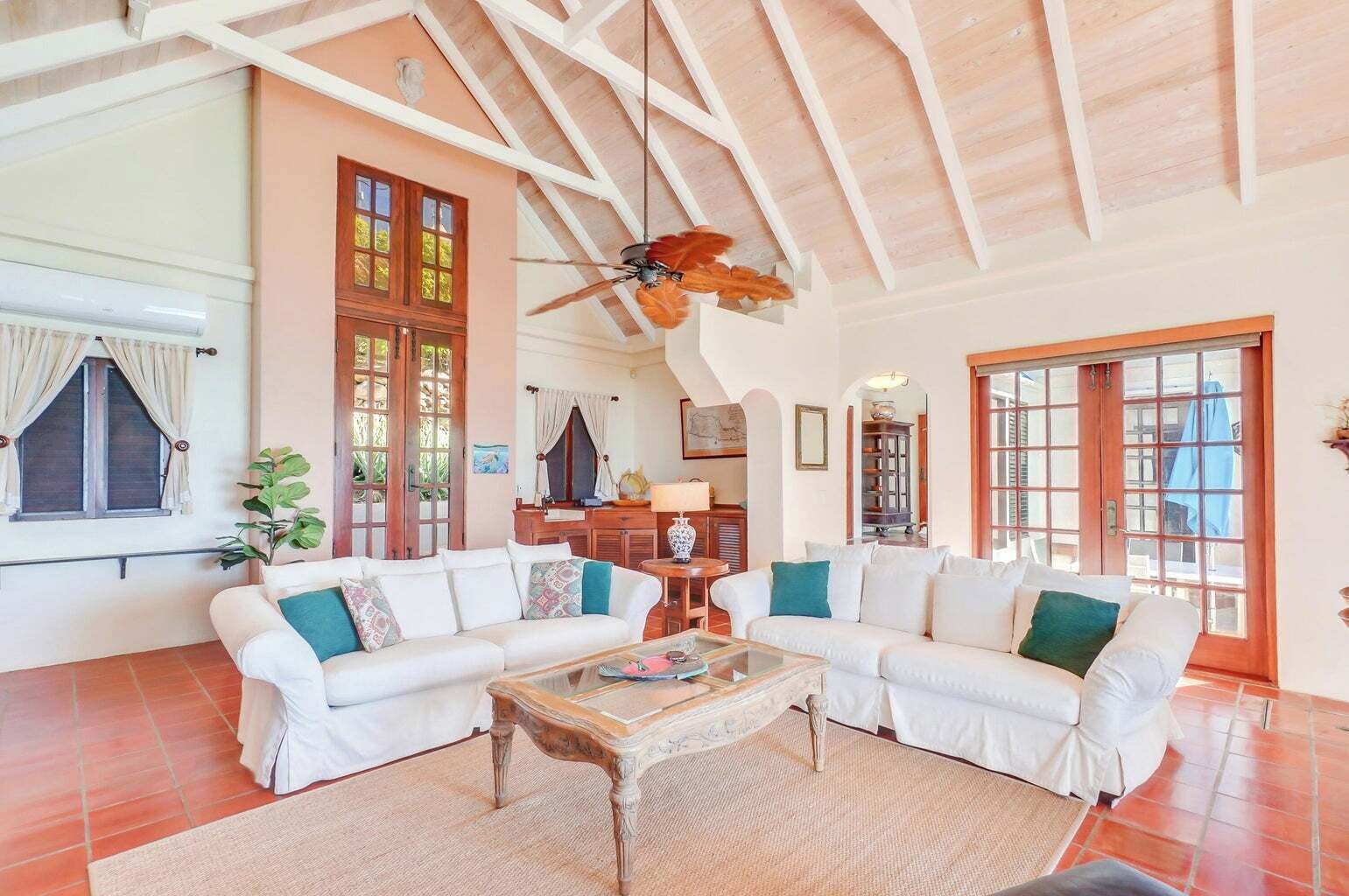 Un salon spacieux avec un plafond haut, un ventilateur de plafond et une grande fenêtre dotée de volets en bois.