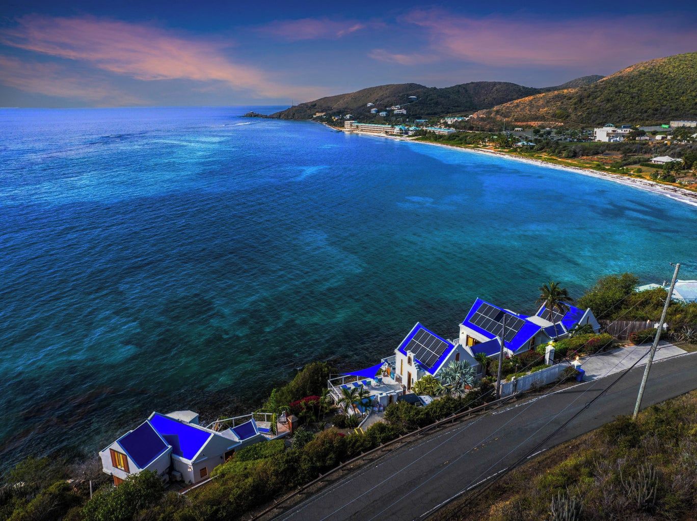 A coastal property with a road leading to a beach, clear blue waters, and houses with blue roofs.
