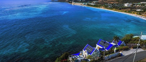 A coastal property with a road leading to a beach, clear blue waters, and houses with blue roofs.