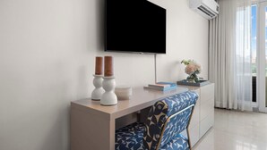 A modern hotel room with a flat-screen TV mounted on the wall, a wooden desk with a chair, and a large window with curtains. - 3BR Lagoon Front Apartment - 2 Private Balconies (San Juan)