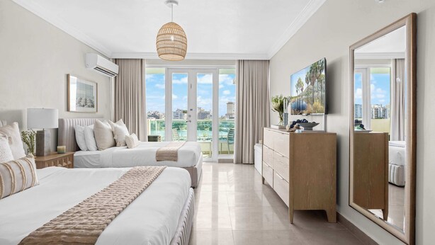 A hotel room with a large bed, a dresser, a mirror, and a view of the city. - 3BR Lagoon Front Apartment - 2 Private Balconies (San Juan)
