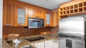 A kitchen with wooden cabinets, a stainless steel microwave, a refrigerator, granite countertops, and a sink. - 3BR Lagoon Front Apartment - 2 Private Balconies (San Juan)