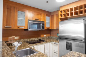 Eine Küche mit Holzausstattung, einer Edelstahl-Mikrowelle, einem Kühlschrank, Granit Arbeitsplatten und einem Spülbecken.