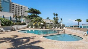 Un hotel con piscina, sillones de descanso y palmeras.